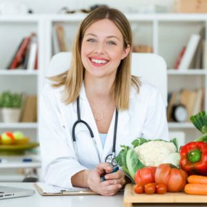 Portrait of beautiful smiling nutritionist looking at camera and showing healthy vegetables in the consultation.